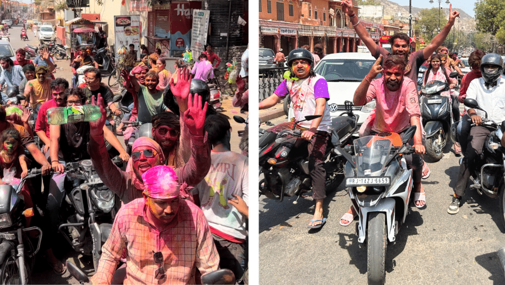 A bustling street scene with numerous people on motorbikes, covered in colorful dust from playing Holi, during festive celebrations in India.